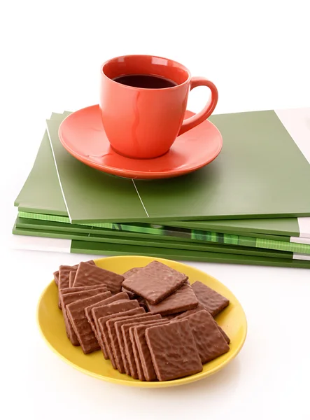 Chocolate cookie and cup of coffee on magazines isolated on whit — Stock Photo, Image