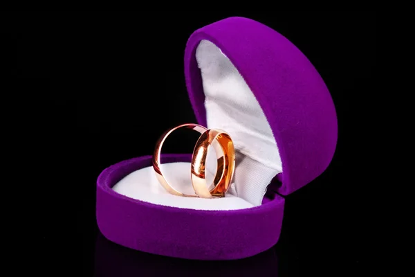 Złote obrączki ślubne w fioletową ramkę na czarnym tle — Zdjęcie stockowe