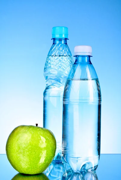 Bottles of water and apple on blue background — Stock Photo, Image