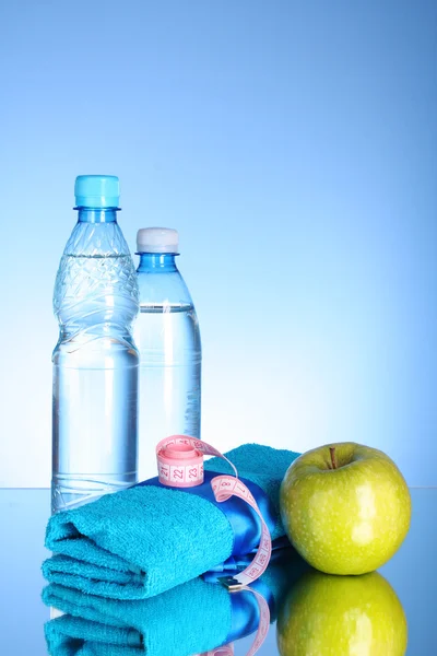 Blue bottle of water, apple, sports towel and measure tape on bl — Stock Photo, Image