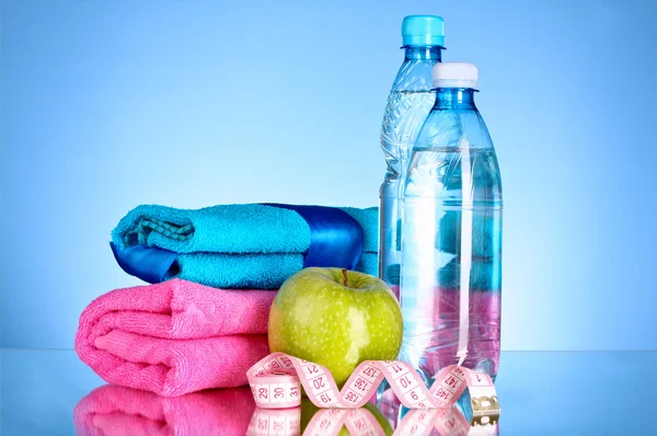 Modrá láhev vody, jablko, sportovní ručník a měření pásky na bl — Stock fotografie