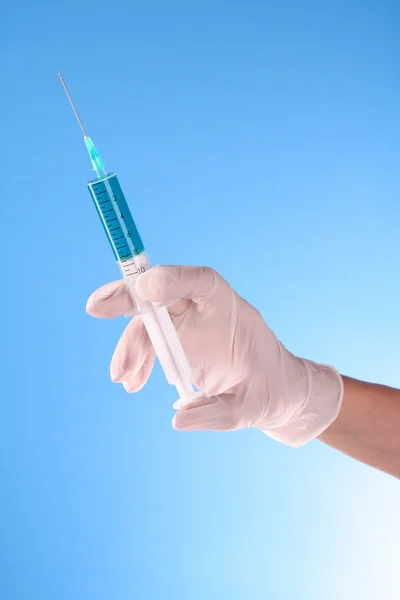 Spruta i läkare hand över blå bakgrund — Stockfoto