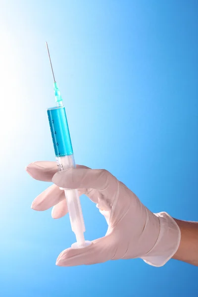 Syringe in artsen hand over blauwe achtergrond — Stockfoto