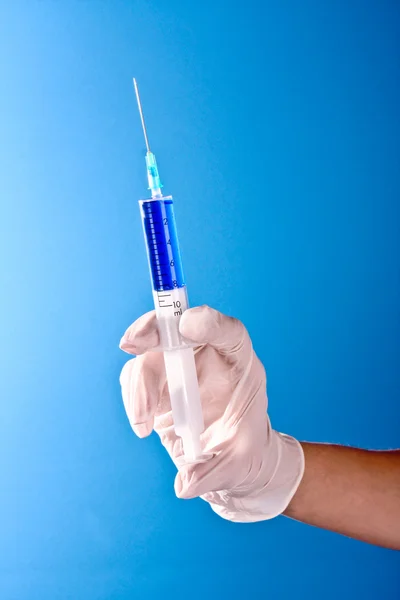 Spruta i läkare hand över blå bakgrund — Stockfoto
