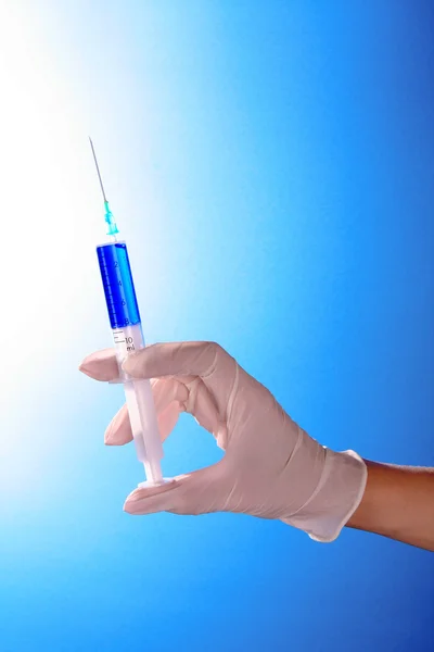 Jeringa en los médicos entregan fondo azul — Foto de Stock