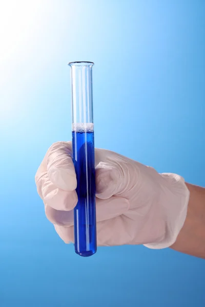 Test tube in hand over blue background — Stock Photo, Image