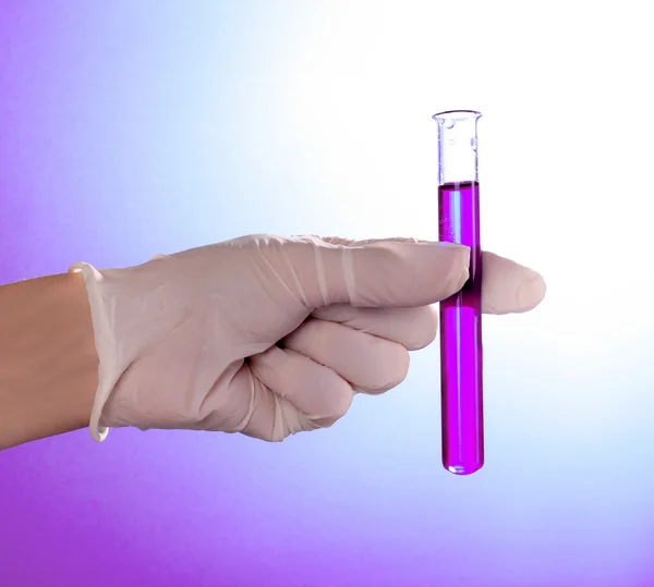 Test tube in hand over violet background — Stock Photo, Image