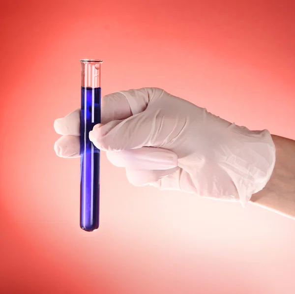 Reagenzglas mit Flüssigkeit in der Hand des Arztes auf rotem Hintergrund — Stockfoto