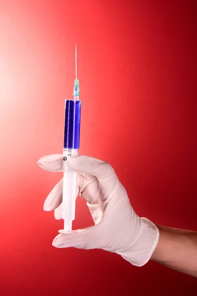 Syringe in doctors hand over red background — Stock Photo, Image