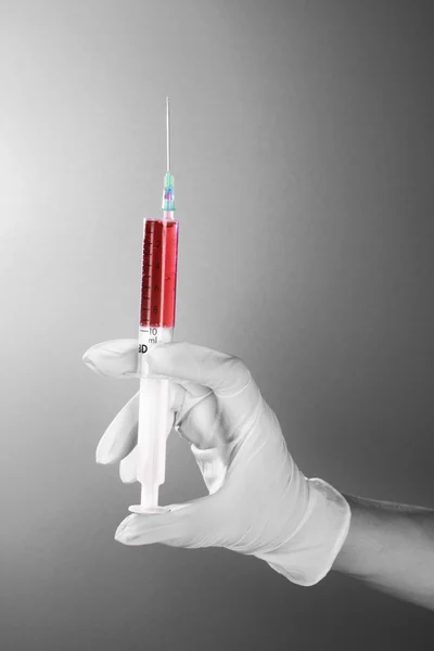 Jeringa con sangre en la mano del médico sobre fondo gris — Foto de Stock