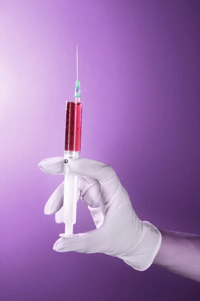 Siringa con sangue nella mano del medico sullo sfondo viola — Foto Stock