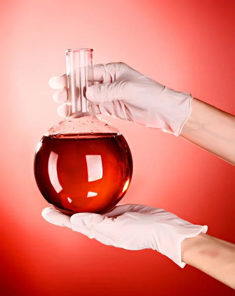 Flask in hand on red background — Stock Photo, Image