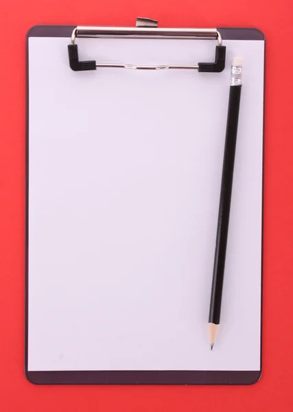 Буфер обмена и карандаш на красном фоне — стоковое фото