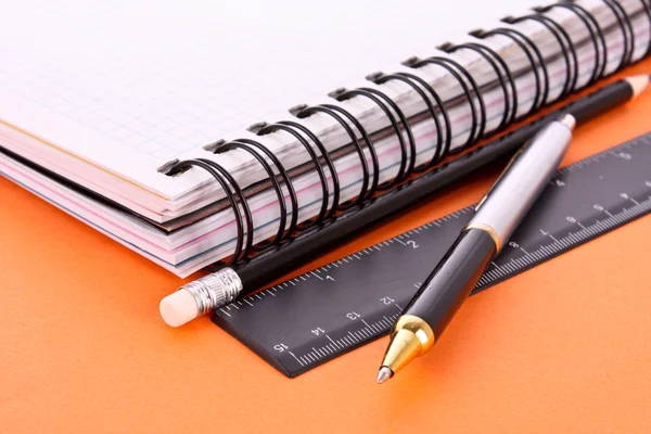Poznámkový blok, tužku, pravítko a pera na oranžovém pozadí — Stock fotografie