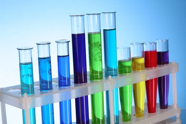Mehrfarbige Reagenzgläser im Stativ auf blauem Hintergrund — Stockfoto