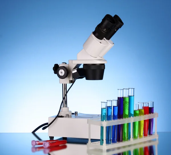 Microscópio de metal de laboratório e tubos de ensaio com líquido em azul b — Fotografia de Stock