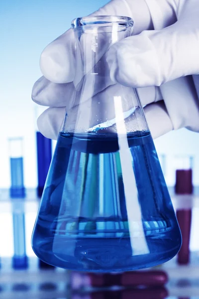 Frasco cónico com líquido azul sobre fundo azul com tubo de ensaio — Fotografia de Stock