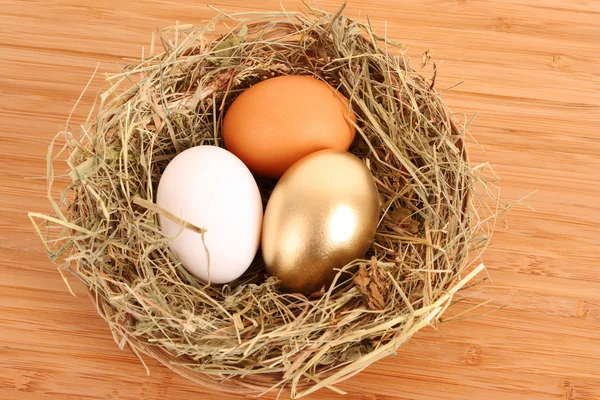 Brązowy, biały i złoty kurze jajko w trawiasta gniazdo na drewnianym tarasem — Zdjęcie stockowe