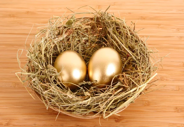 Trzy złote kurze jaja w gnieździe trawiastych na drewnianym stole — Zdjęcie stockowe