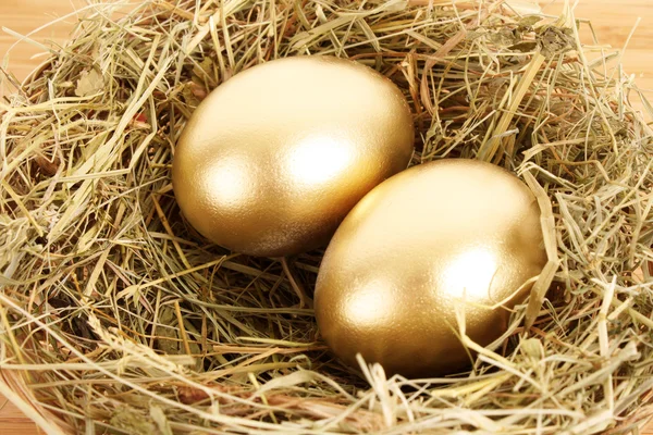 Три золотых куриных яйца в травянистом гнезде на деревянном столе — стоковое фото