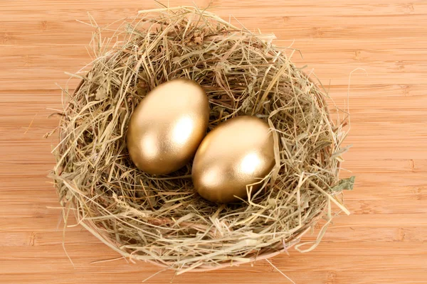 Três ovos de galinha dourada no ninho gramado na mesa de madeira — Fotografia de Stock