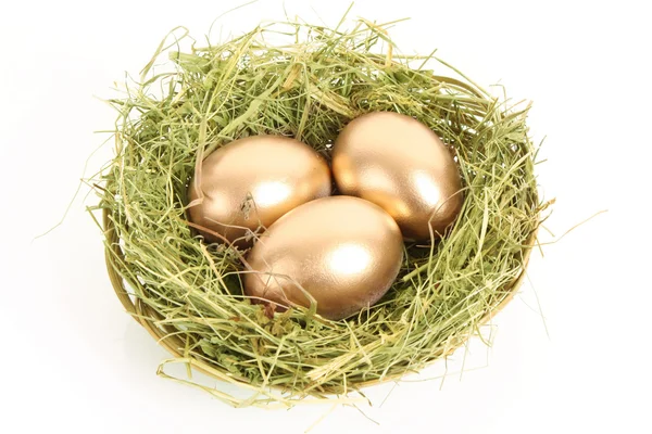 Trzy złote kurze jaja w gnieździe trawiastych na białym tle — Zdjęcie stockowe