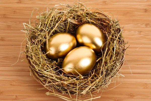 Three golden hen's eggs in the grassy nest on the wooden table — Stock Photo, Image