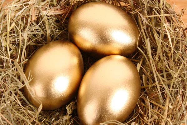 Tři zlaté vejce, v travnatých hnízdo na dřevěný stůl — Stock fotografie