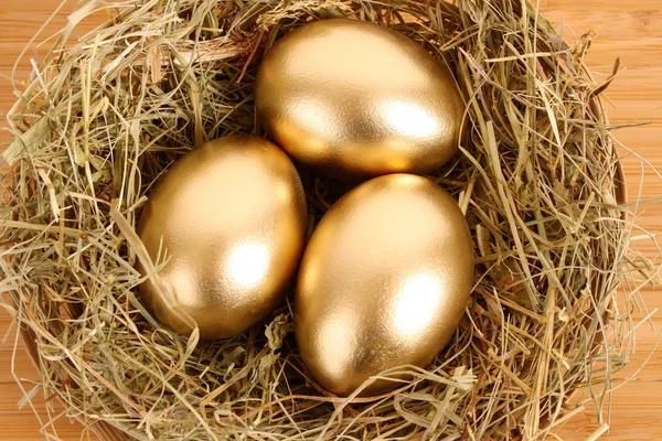 Ahşap masa üzerinde çimenli yuvadaki üç altın tavuk yumurta — Stok fotoğraf