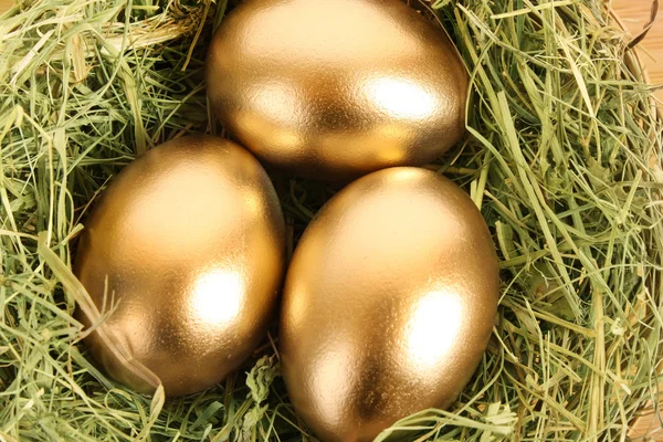 Tři zlaté vejce, v travnatých hnízdo na dřevěný stůl — Stock fotografie