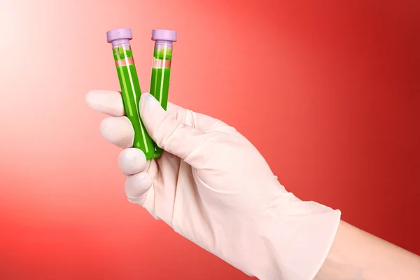 Test tubes with fluid in hand on red background — Stock Photo, Image