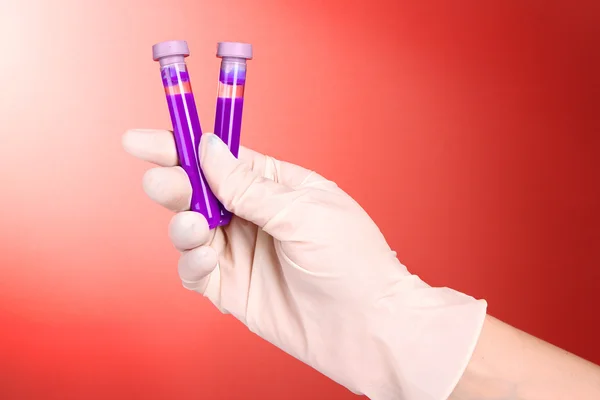 Test tubes with fluid in hand on red background — Stock Photo, Image