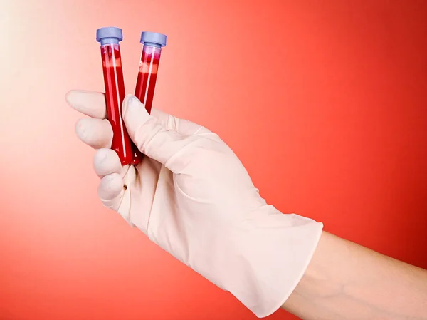 Mão de médico em luva com tubos de teste de sangue em fundo vermelho — Fotografia de Stock