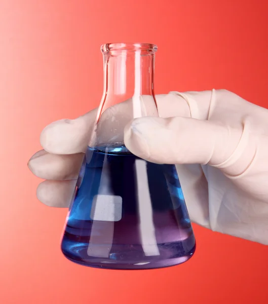 Beaker with blue liquid on hand with red background — Stock Photo, Image