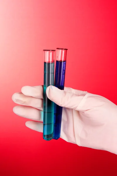 Tubos de ensaio com fluido à mão sobre fundo vermelho — Fotografia de Stock
