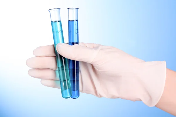 Tubos de ensaio com fluido à mão sobre fundo azul — Fotografia de Stock