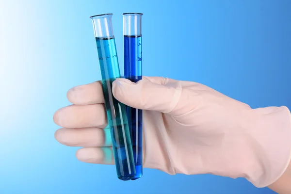 Tubos de ensaio com fluido à mão sobre fundo azul — Fotografia de Stock
