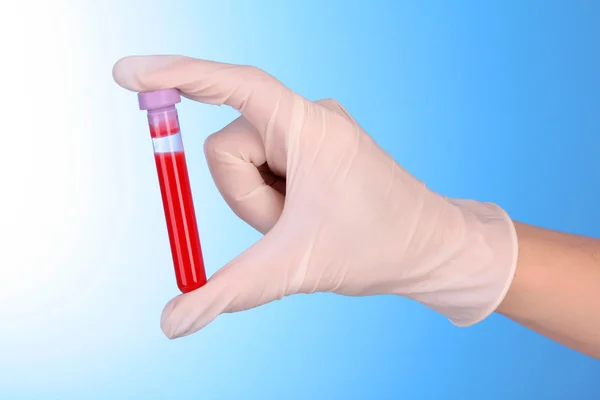 Test tube with blood in hand over blue background — Stock Photo, Image
