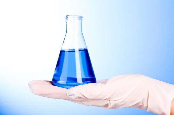 Bekerglas met blauwe vloeistof op hand met blauwe achtergrond — Stockfoto