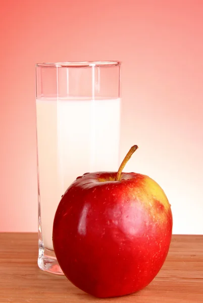 Rött äpple och mjölk på en monter med röd bakgrund — Stockfoto
