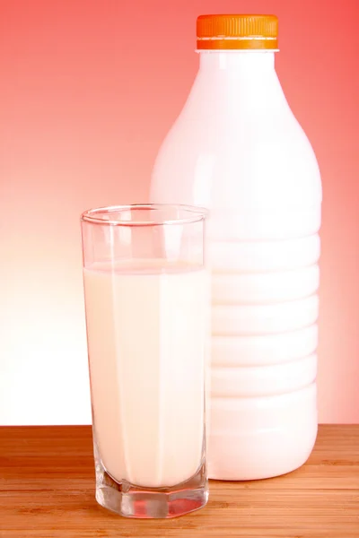 Verre de lait et bouteille sur fond rouge — Photo