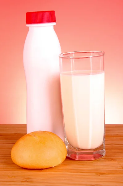 Láhev mléka, bochník a skla na červeném pozadí — Stock fotografie