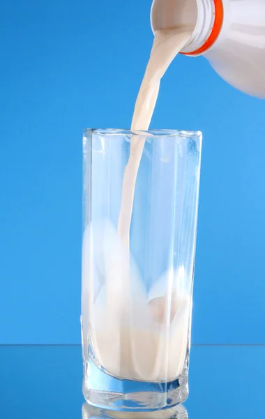 Alguém despeje leite em vidro no fundo azul — Fotografia de Stock