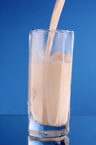 Někdo nalít mléko ve skle na modrém pozadí — Stock fotografie