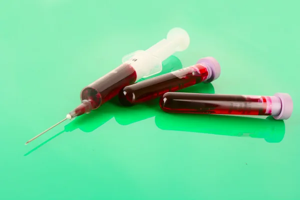 Zkumavky lékařské a stříkačka s krví na zelené — Stock fotografie