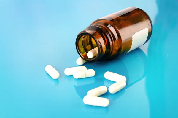 Garrafa pílula com pílulas brancas em azul — Fotografia de Stock