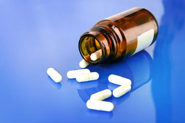 Pill bottle with white pills on blue — Stock Photo, Image