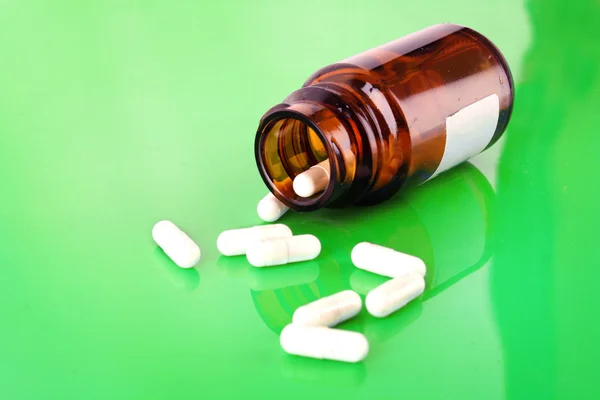 Pilulku láhev s bílými prášky na zelené — Stock fotografie