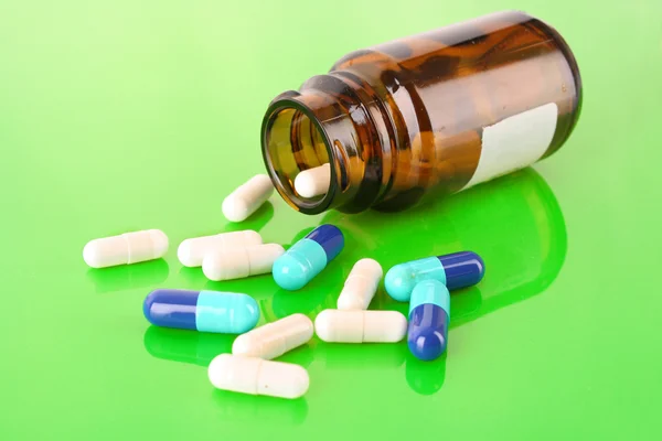 Frasco de la píldora con píldoras blancas y azules en verde —  Fotos de Stock