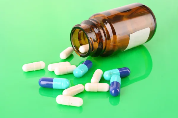 Pill bottle with white and blue pills on green — Stock Photo, Image